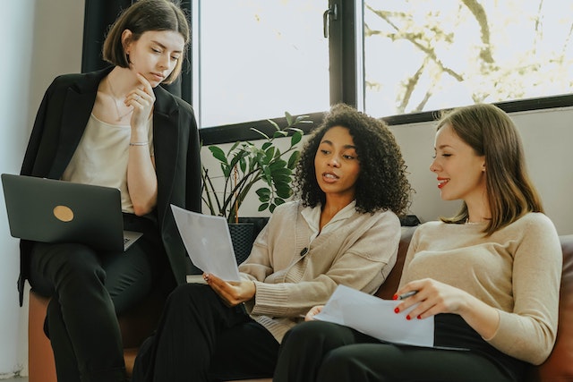 Three people sittign on a sofa together while lokoing at printed documents and talking