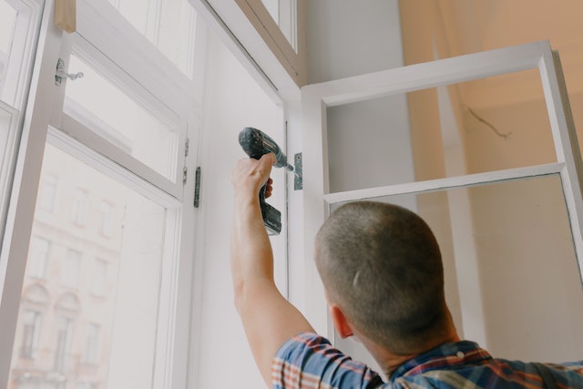 Person drilling in the hinges of a white window